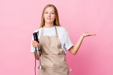 Genç Rus aşçı kadın bir elektrikli mikser tutuyor. Kafası karışık ve omuz silkiyor. Kopya alanını tutmak için..