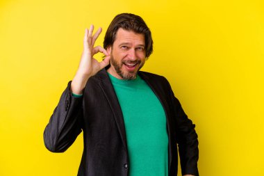 Orta yaşlı beyaz bir adam sarı arka planda izole edilmiş bir şekilde göz açıp kapayıncaya kadar iyi bir jest yapıyor..