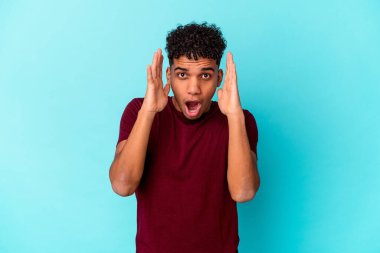 Genç Afro-Amerikalı kıvırcık adam mavi üzerine izole edilmiş şaşırmış ve şok olmuş..