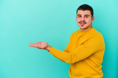 Mavi arka planda izole edilmiş genç beyaz bir adam palmiyesinde bir kopya alanı tutuyor..