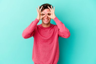 Kafkasyalı genç adam mavi arka planda izole edildi. Heyecanlı görünüyor..