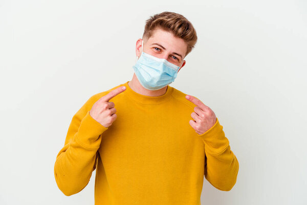 Young man wearing a mask for coronavirus isolated on white background smiles, pointing fingers at mouth.