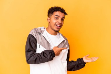 Genç Afro-Amerikalı kıvırcık adam, mor renkte izole edilmiş. Elinde palmiye ağacının bir kopyası var..