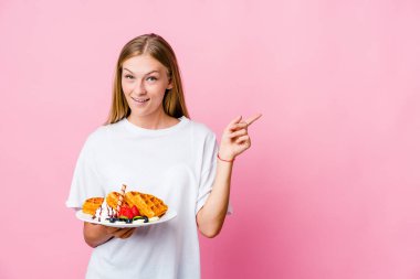 Genç Rus kadın yalnız başına waffle yiyor. Gülümsüyor, işaret parmağıyla işaret ediyor..