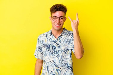 Sarı arka planda izole edilmiş genç beyaz adam parmaklarıyla kaya hareketi gösteriyor.