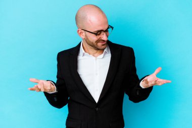 Genç beyaz, kel bir adam mavi arka planda izole edilmiş. Elinde avuç içi olan bir şey var. Kameraya teklif ediyor..