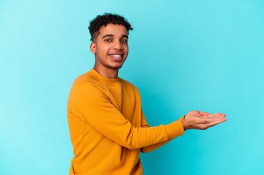 Genç Afro-Amerikalı kıvırcık adam mavi üzerine izole edilmiş. Elinde palmiye üzerinde bir kopya alanı var..