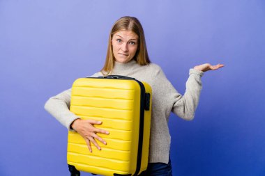 Genç Rus kadın seyahat etmek için bavul tutuyor. Kafası karışık ve kopya alanı tutmak için omuz silkiyor..