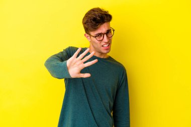 Sarı arka planda izole edilmiş genç beyaz adam tiksinti belirtisi gösteren birini reddediyor..