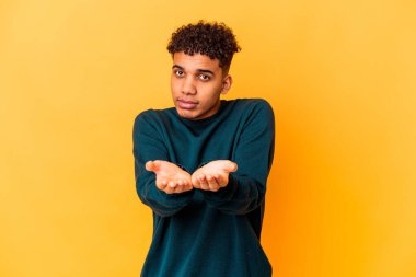 Genç Afro-Amerikalı kıvırcık adam, mor üzerine izole edilmiş, elinde avuç içi olan bir şeyle kameraya sunuyor..