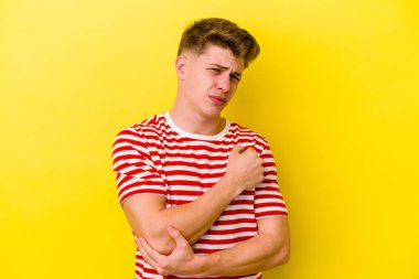 Genç beyaz adam sarı arka planda izole edilmiş dirsek masajı yapıyor, kötü bir hareketin ardından acı çekiyor..