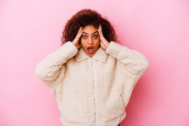 Pembe arka planda izole edilmiş genç Afro-Amerikalı kadın yüzünün yarısını palmiye ile örterek eğleniyor..