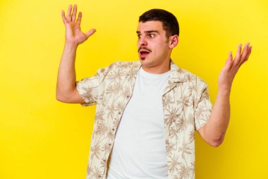 Sarı arka planda izole edilmiş genç beyaz adam gökyüzüne haykırıyor, yukarı bakıyor, hayal kırıklığına uğramış..