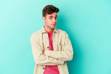 Mavi arka planda izole edilmiş genç beyaz adam alaycı bir ifadeyle kameraya bakarken mutsuz oluyor..