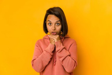 Genç İspanyol kadın sarıda izole edilmiş, şans için dua ediyor, şaşırmış ve ağzını açıp önüne bakıyor..