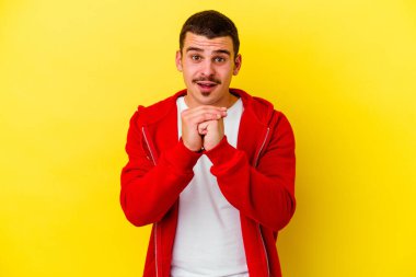 Beyaz tenli genç adam sarı arka planda izole edilmiş şans için dua ediyor, şaşırmış ve ağzını açıp önüne bakıyor..