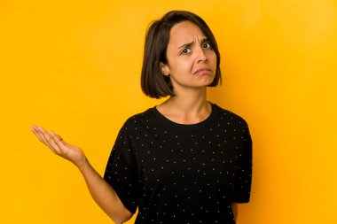 Genç İspanyol kadın sarı renkte izole edilmiş şüpheyle ve omuz silkerek jestini sorguluyor..