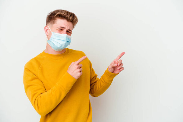 Young man wearing a mask for coronavirus isolated on white background pointing with forefingers to a copy space, expressing excitement and desire.