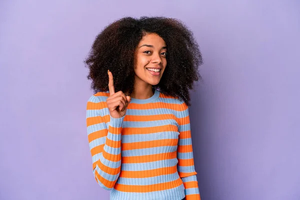 紫色の背景に孤立した若いアフリカ系アメリカ人の巻き毛の女性は指でナンバーワンを示す — ストック写真