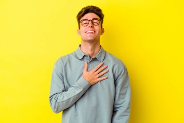 Sarı arka planda izole edilmiş genç beyaz adam yüksek sesle gülüyor ve elini göğsüne koyuyor..