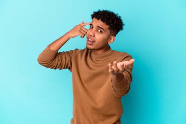 Genç Afro-Amerikalı kıvırcık adam mavi salonda izole edilmiş ve elinde bir ürün var..