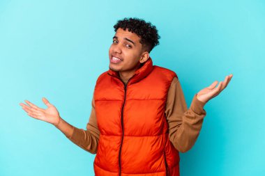 Genç Afro-Amerikalı kıvırcık adam mavi üzerine izole edilmiş. Kafası karışmış ve omuz silkiyor. Kopya alanını tutmak için..