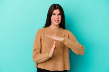 Mavi arka planda izole edilmiş genç beyaz kadın bir mola hareketi gösteriyor..