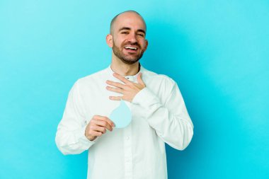 Kafkasyalı genç kel adam dünya gününü kutluyor mavi arka planda izole edilmiş su günü kahkahalar atıyor göğsünde elini tutuyor.