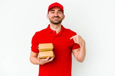 Beyaz arka planda izole edilmiş beyaz tenli genç teslimatçı gömlek fotokopi alanını gösteriyor, gururlu ve kendinden emin.