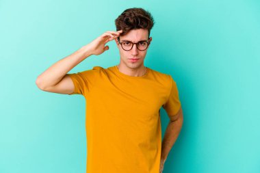 Mavi arka planda izole edilmiş genç beyaz bir adam şakağı parmağıyla işaret ediyor, düşünüyor ve bir göreve odaklanıyor..