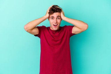 Genç beyaz adam mavi arka planda izole edilmiş bağırıyor, çok heyecanlı, tutkulu, bir şeyden memnun..