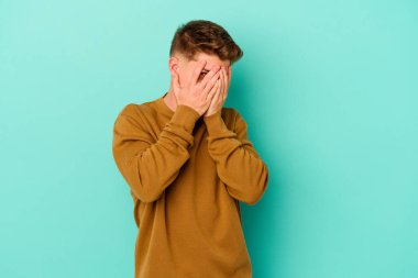 Kafkasyalı genç adam mavi arka planda izole edilmiş. Korkmuş ve gergin parmaklarıyla göz kırp..