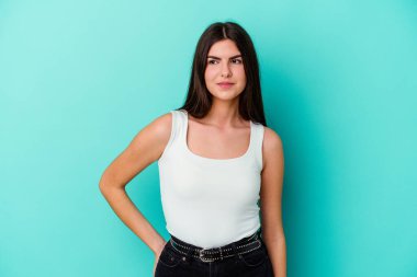 Kafkasyalı genç bir kadın mavi arka planda izole edilmiş, kafası karışmış, şüpheli ve kendinden emin değil..