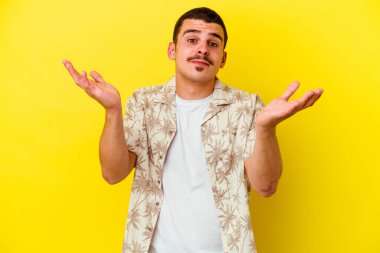 Kafkas asıllı genç adam sarı arka planda izole edilmiş. Kafası karışmış ve omuz silkiyor. Kopya alanını tutmak için..