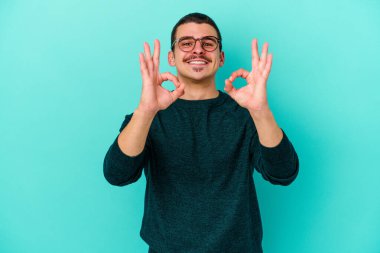 Kafkasyalı genç adam mavi arka planda izole edilmiş neşeli ve kendinden emin..