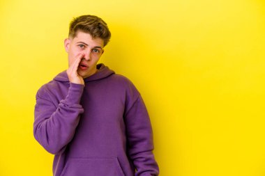 Sarı arka planda izole edilmiş genç beyaz bir adam gizli bir sıcak fren haberi veriyor ve yana bakıyor.