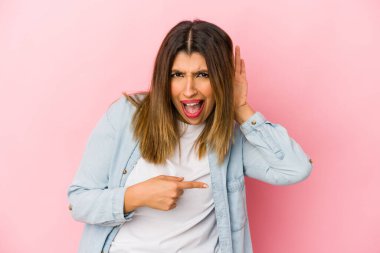 Pembe arka planda izole edilmiş genç Hintli kadın bir dedikoduyu dinlemeye çalışıyor..