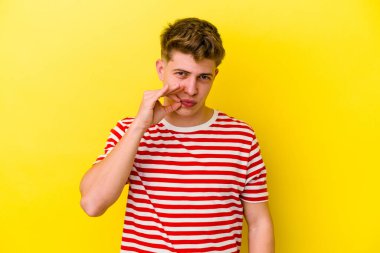 Sarı arka planda izole edilmiş genç beyaz bir adam parmakları dudaklarında bir sır saklıyor..