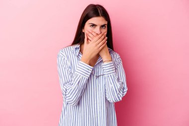 Pembe arka planda izole edilmiş genç, beyaz bir kadın elleri endişeli bir şekilde ağzı örtüyor..