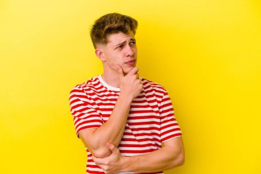 Kafkasyalı genç adam sarı arka planda izole edilmiş düşünüyor ve yukarı bakıyor, yansıtıyor, düşünüyor, hayal kuruyor..