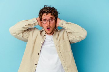 Mavi arka planda izole edilmiş gözlük takan genç beyaz adam çığlık atıyor, çok heyecanlı, tutkulu, bir şeyden memnun..