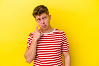 Kafkasyalı genç adam sarı arka planda izole edilmiş, ağlıyor, bir şeyden memnun değil, acı ve kafa karışıklığı kavramı..