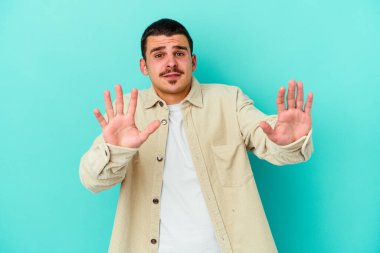 Mavi arka planda izole edilmiş genç beyaz adam tiksinti belirtisi gösteren birini reddediyor..