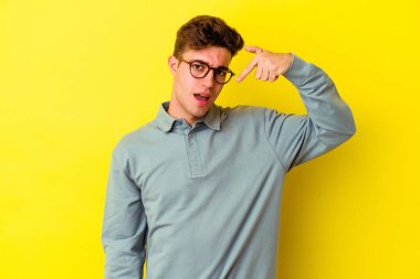 Sarı arka planda izole edilmiş genç beyaz bir adam gömlek fotokopi alanını elle gösteriyor, gururlu ve kendinden emin.