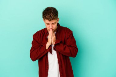 Kafkasyalı genç adam mavi arka planda izole edilmiş dua ediyor, bağlılık gösteriyor, dindar biri ilahi ilham arıyor..