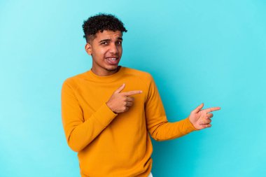 Genç Afro-Amerikalı kıvırcık adam mavi üzerine izole edilmiş, işaret parmağıyla fotokopi alanını işaret ediyor..