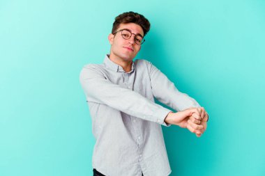 Mavi arka planda izole edilmiş genç beyaz adam kollarını uzatıyor, rahat bir konumda..