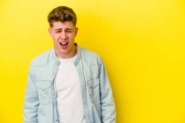 Sarı arka planda izole edilmiş genç beyaz bir adam çok kızgın, öfkeli, hayal kırıklığına uğramış diye bağırıyor..