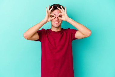 Mavi arka planda izole edilmiş genç beyaz adam gözlerinde sorun olmadığını gösteriyor.