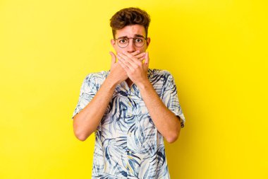 Sarı arka planda izole edilmiş genç beyaz adam elleriyle ağzını kapatırken şok oldu..